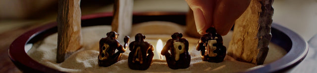 A bowl with 4 apes sitting round a small night light flame. There are stone menhirs that have been stuck into the sand that fills the bowl. Each ape has a letter on its back that spells BAPE